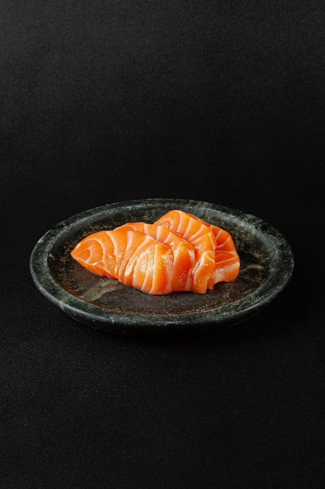 Fatias frescas de sashimi de salmão empilhadas em prato de pedra escura