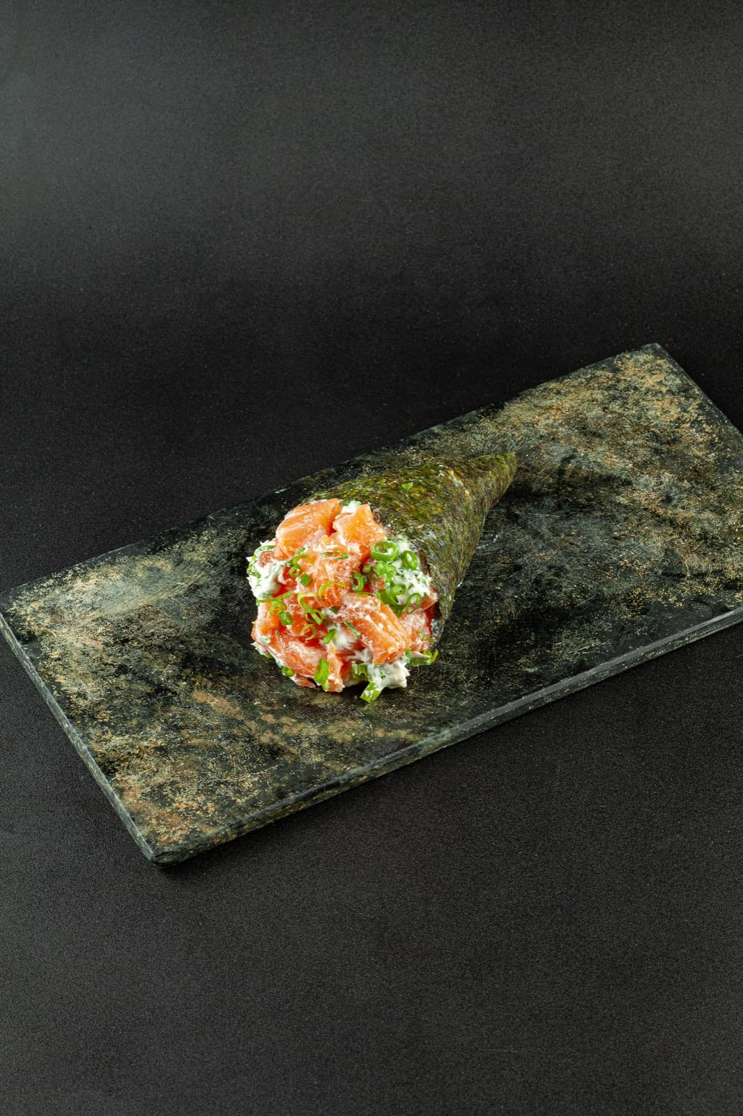 Temaki de salmão com cream cheese e cebolinha recém-enrolado, servido na pedra
