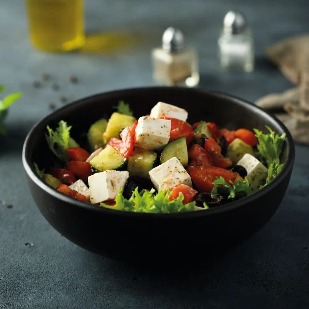Salada de folhas com queijo, pepino e tomate em tigela preta