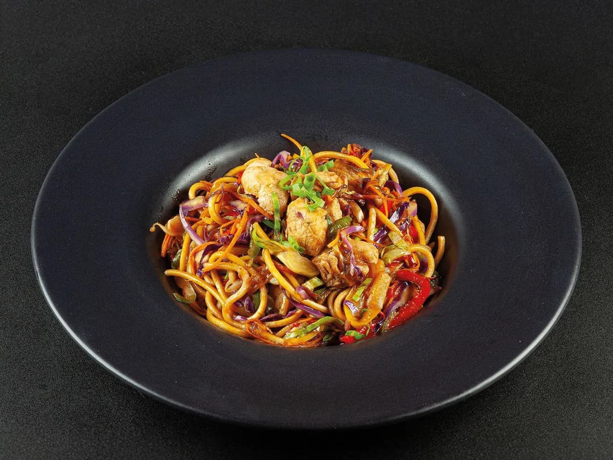 Yakissoba de frango com legumes em prato fundo preto